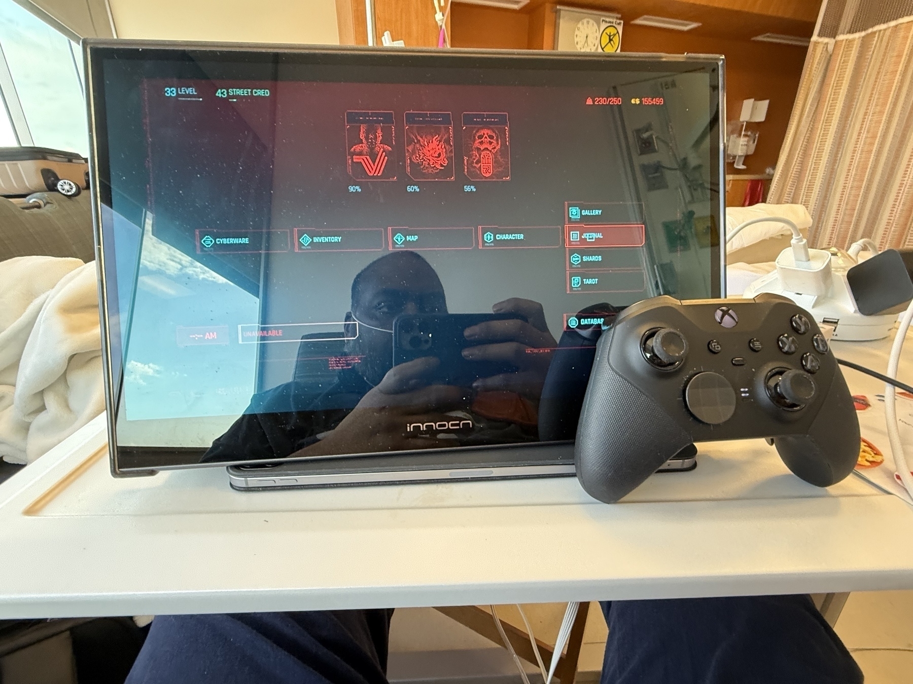 External monitor displaying Cyberpunk 2077. An Xbox Elite controller balanced on the monitor