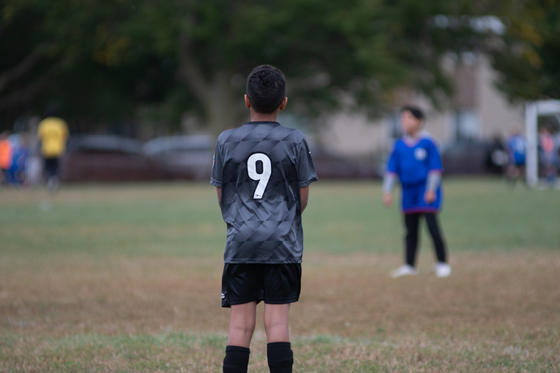 A young soccer player wearing a jersey with the number 9 stands on a field, focusing on the game.