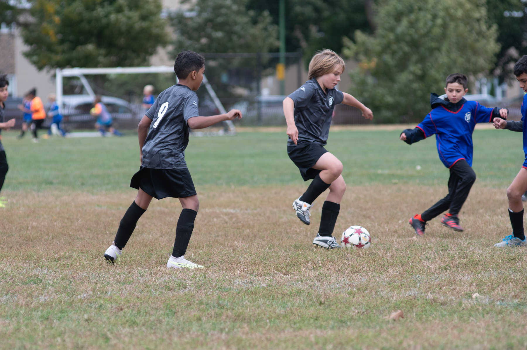 Young boys are playing soccer on a grassy field, with one player dribbling the ball.