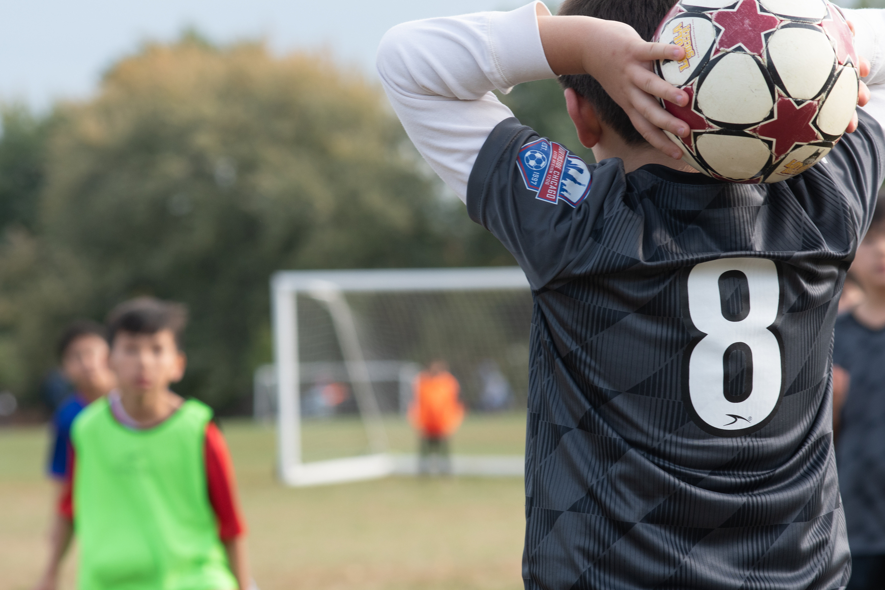 A young soccer player wearing a black jersey with the number 8 is preparing to throw the ball back into play during a game.